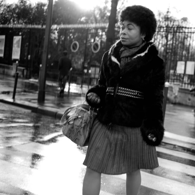 a woman in a coat and skirt stands on the side walk