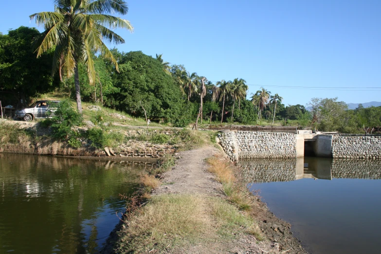 a dirt path going beside a canal near a bridge