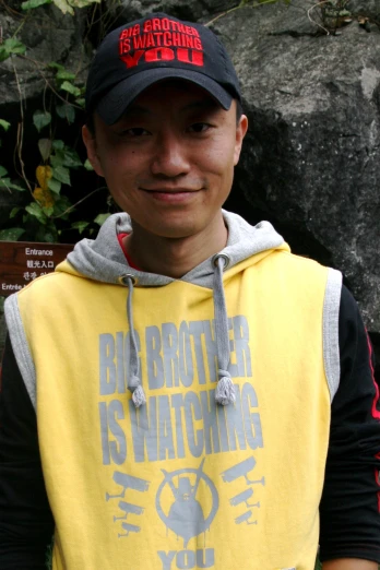 man wearing a yellow and black hooded sweatshirt next to a rock