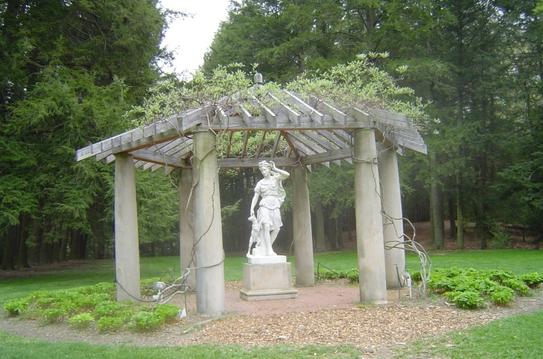 a statue in front of a wooden gazebo with a stone sculpture at the base