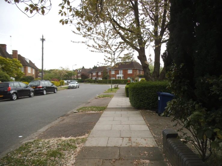 a sidewalk that leads to the street where several parked cars are parked