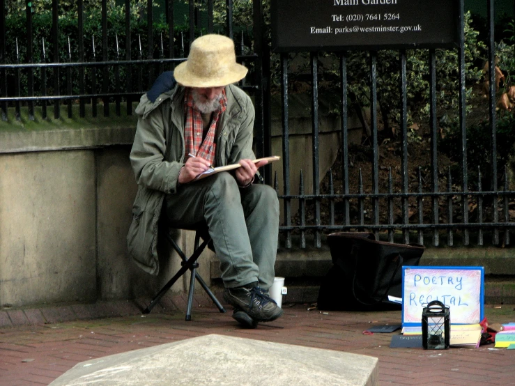 man sitting down next to a plaque and writing on a stick