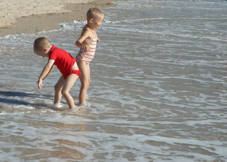 two children play in shallow water at the edge of a beach