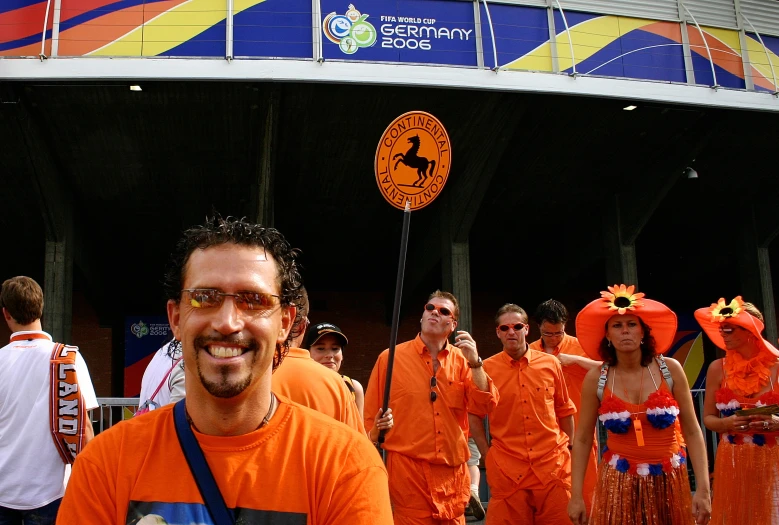 a man wearing orange and an orange dress walks along a street in front of people dressed in orange and blue