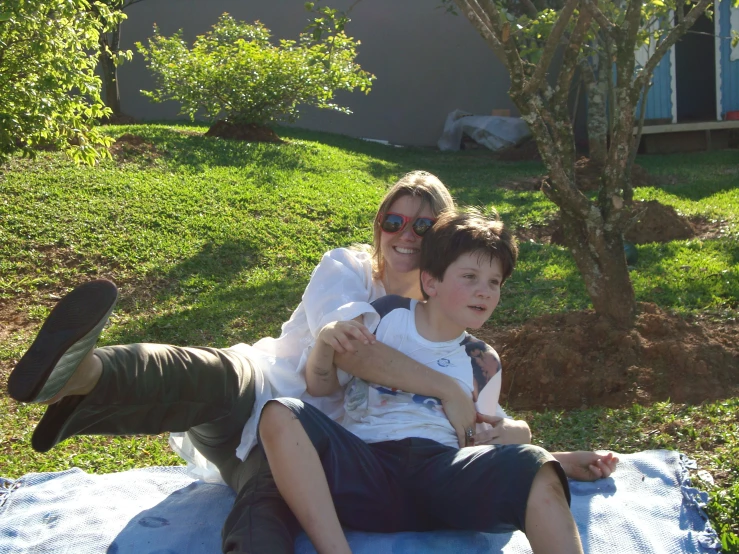 the mother and son are sitting on the blanket outside