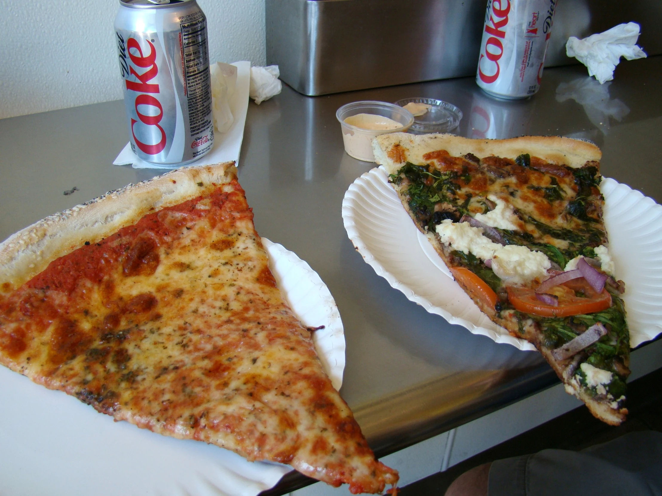 there is one slice of pizza on a plate and two cans of coke