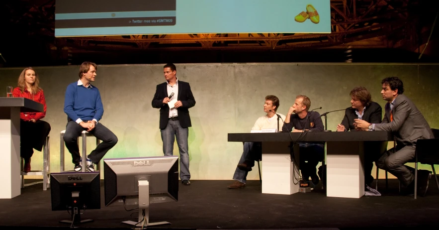 four men sitting at tables while two women stand on the stage