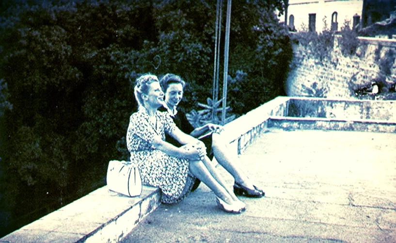 two women sitting on the side of a balcony with a view of water and trees