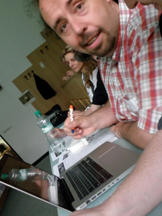 two men and a woman look over a bottle of water and laptop computer