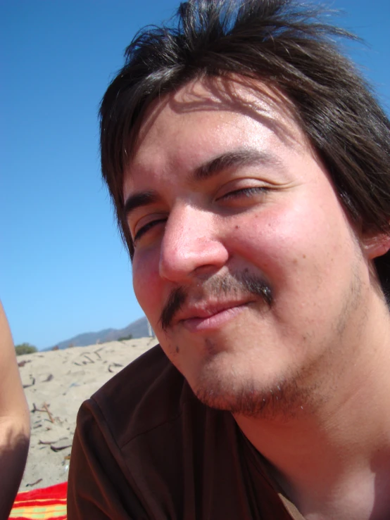 a man wearing a brown shirt and mustache smiles at the camera