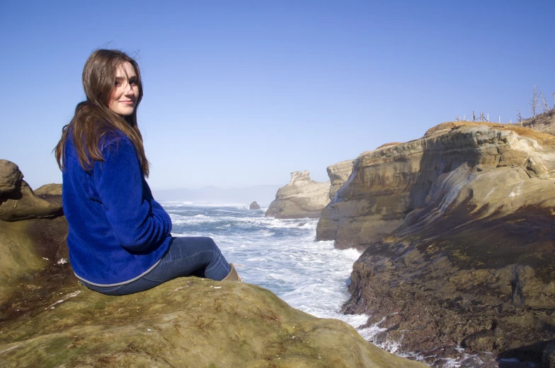 the woman sits on top of a rock near the ocean