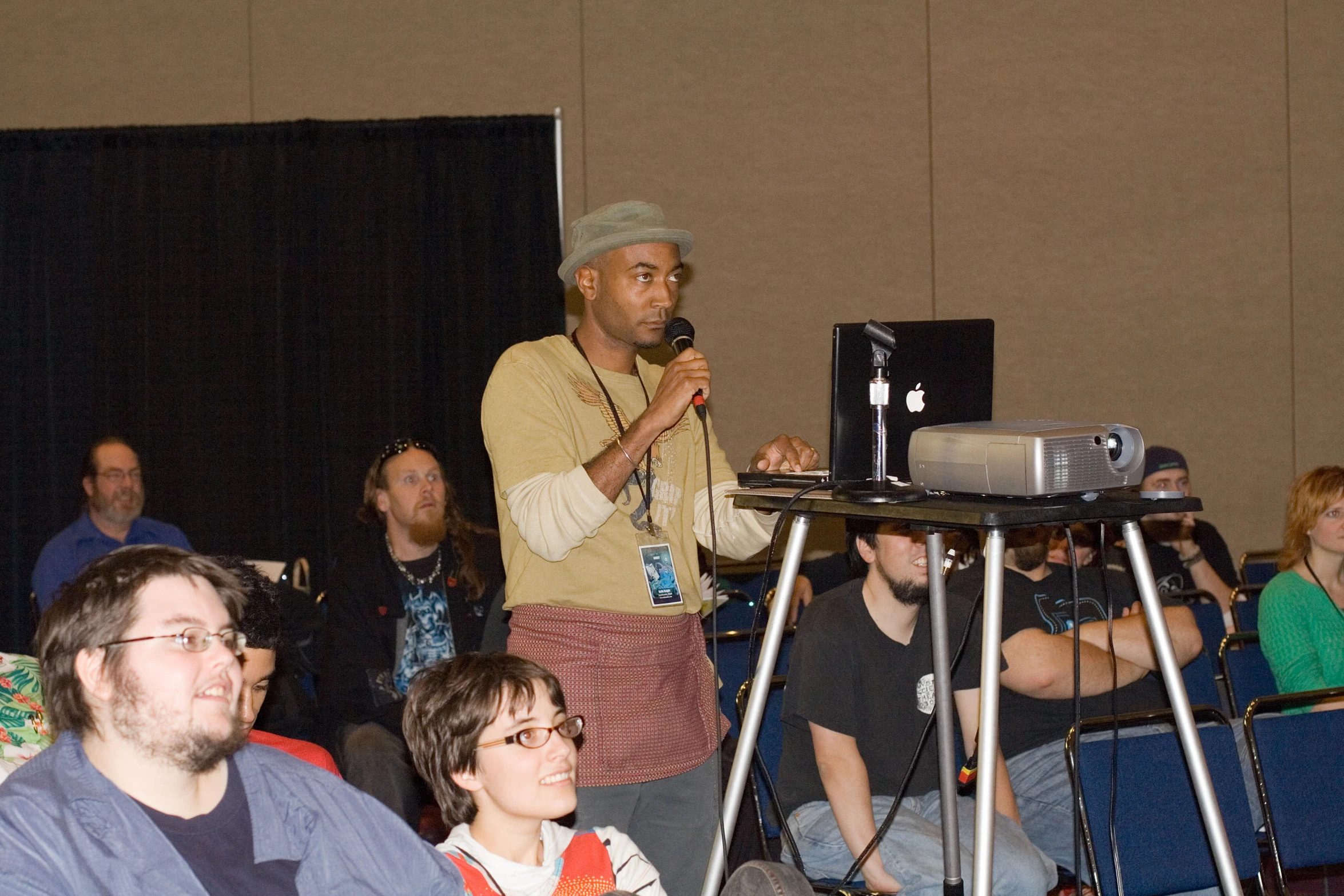 a man on a stage holds a microphone while listening to a group of people