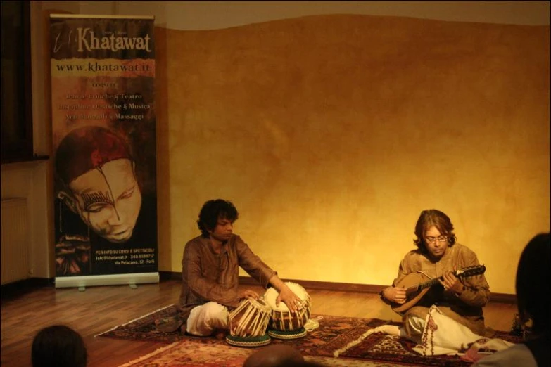 two people sitting on the ground next to each other playing guitars