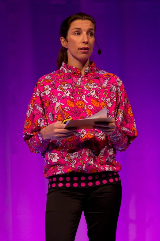 woman in a colorful shirt standing on stage with notebook