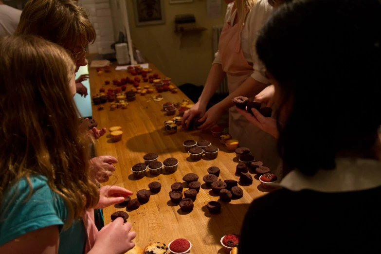 children and adults are at a table with many cupcakes