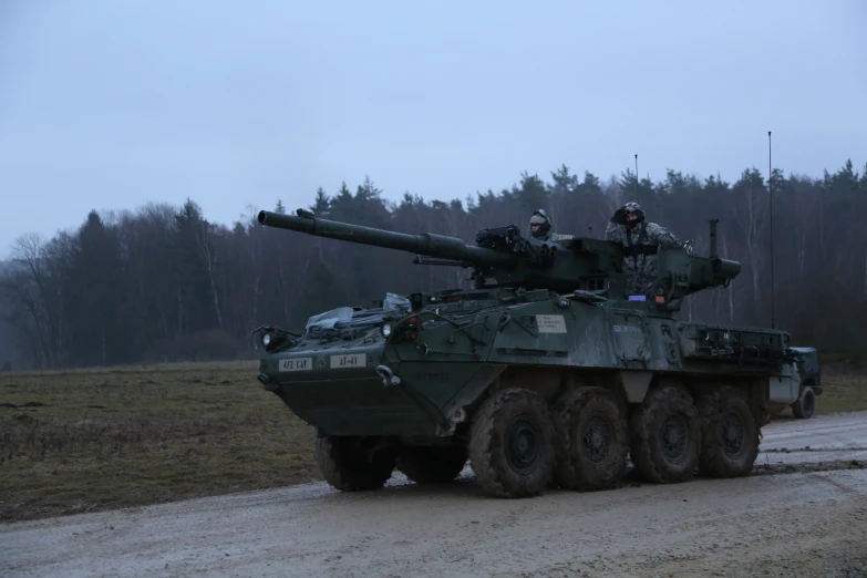 a tank is driving down the road as people look out on the grassy land behind it