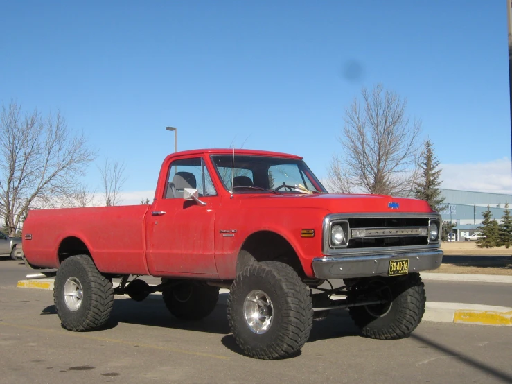 a red pickup truck with a huge wheel driving down the road