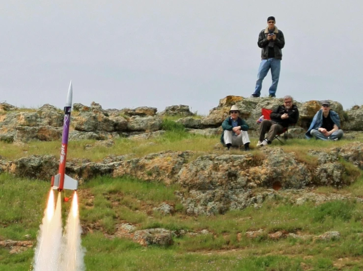 people sitting on a hill, looking at a rocket