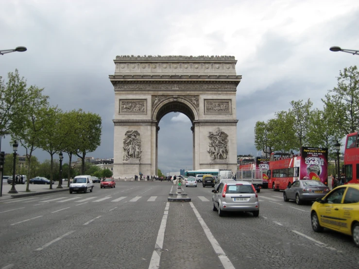 a bus, truck and motorcycle are driving in front of the arc triumph