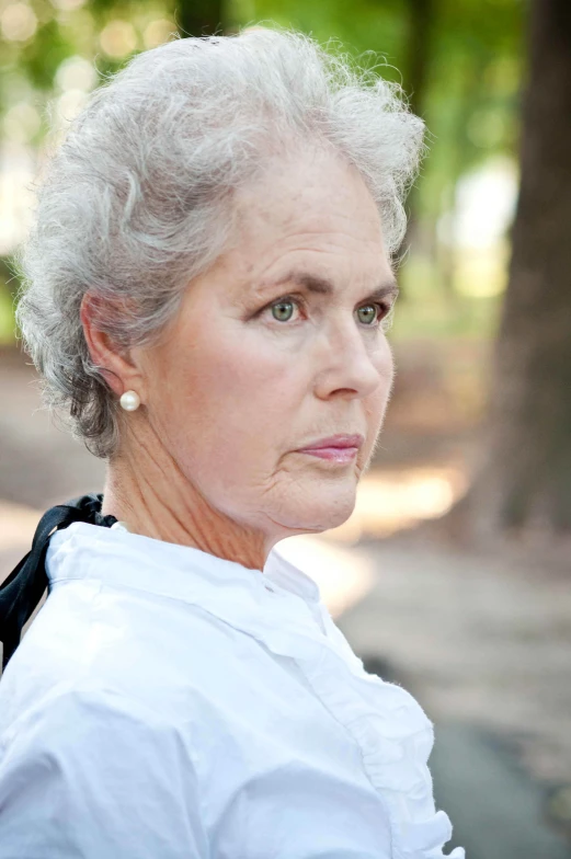 the older woman is wearing white clothes in front of some trees