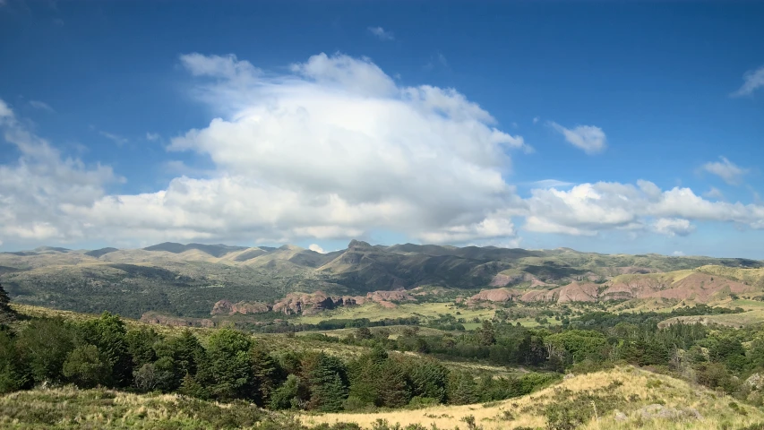 a green hillside covered in hills under cloudy skies