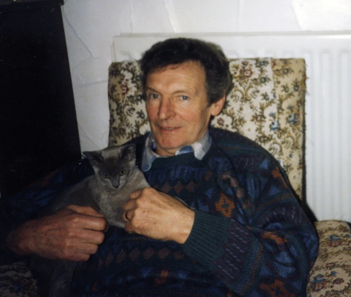 an elderly man is sitting in a chair holding a cat