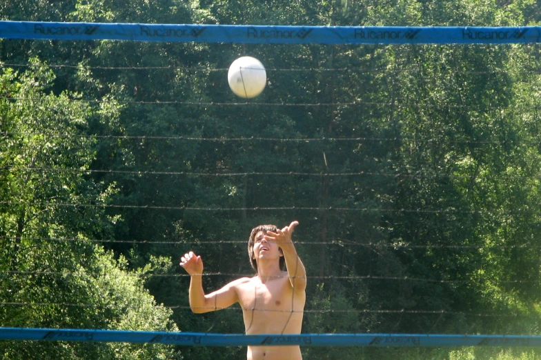 the shirtless young man is playing volleyball in the woods