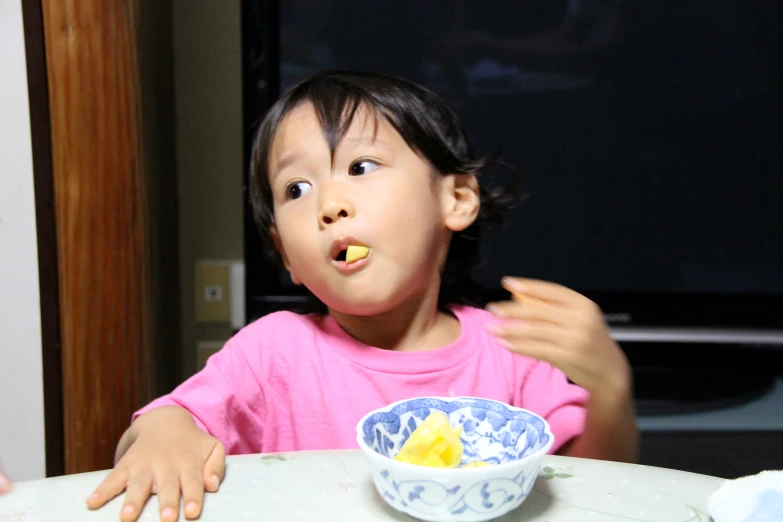 a little girl in a pink shirt eating a piece of food with her hands