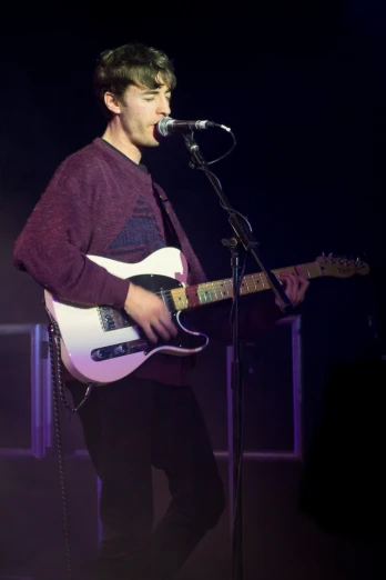 a man in maroon sweater and white guitar singing into microphone