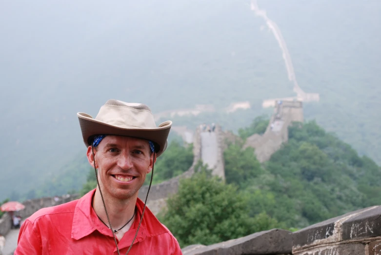 a man in a cowboy hat poses near the great wall of china