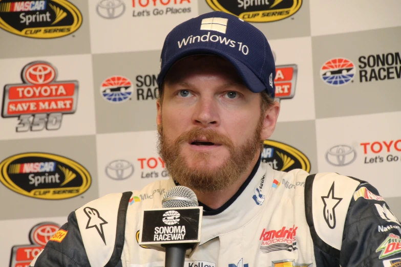 a man talking into a microphone next to a wall with other nascar sponsors