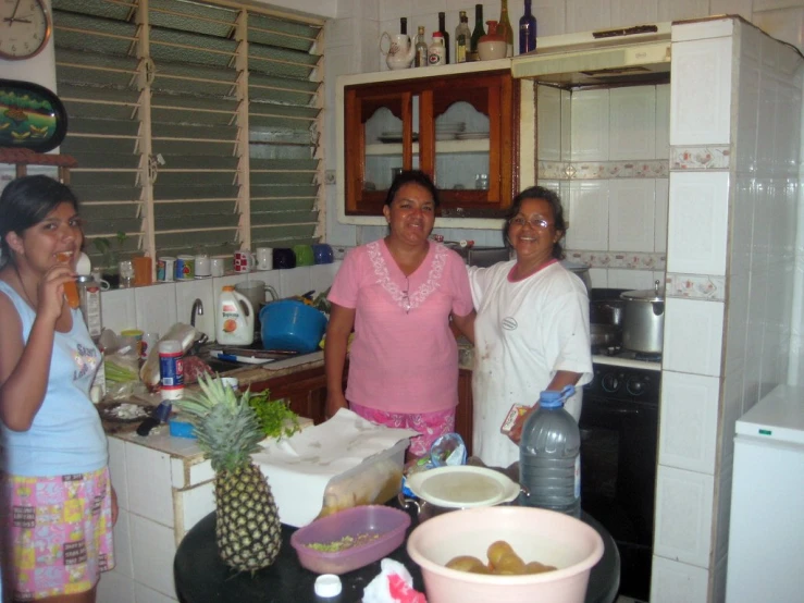 three women in a small kitchen with one holding a plastic bottle