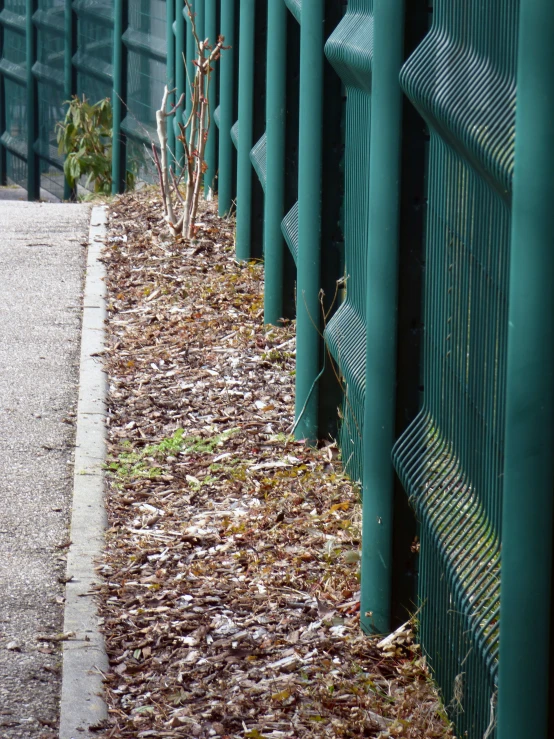 a close up s of a green metal fence next to a dirt sidewalk