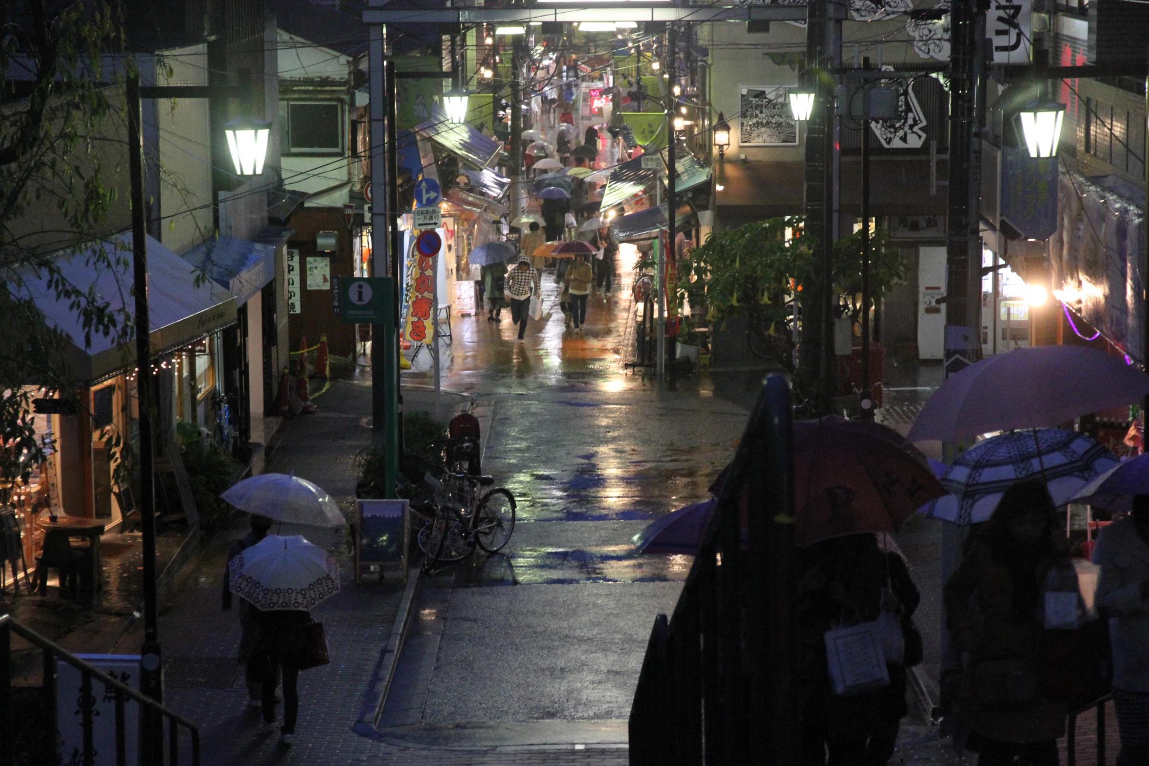 people with umbrellas are walking down a rainy street