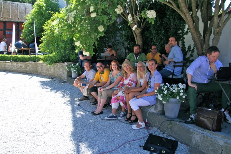 people seated on the stone wall near trees, shrubs and flowers