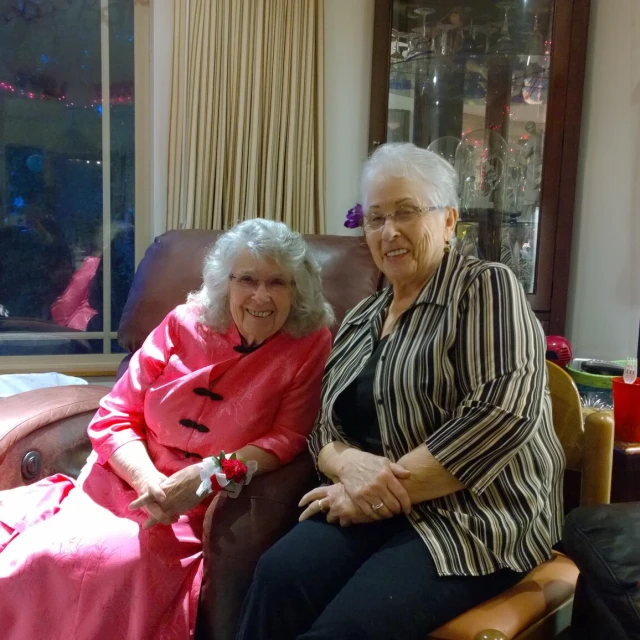 two older women pose for the camera while sitting on the couch