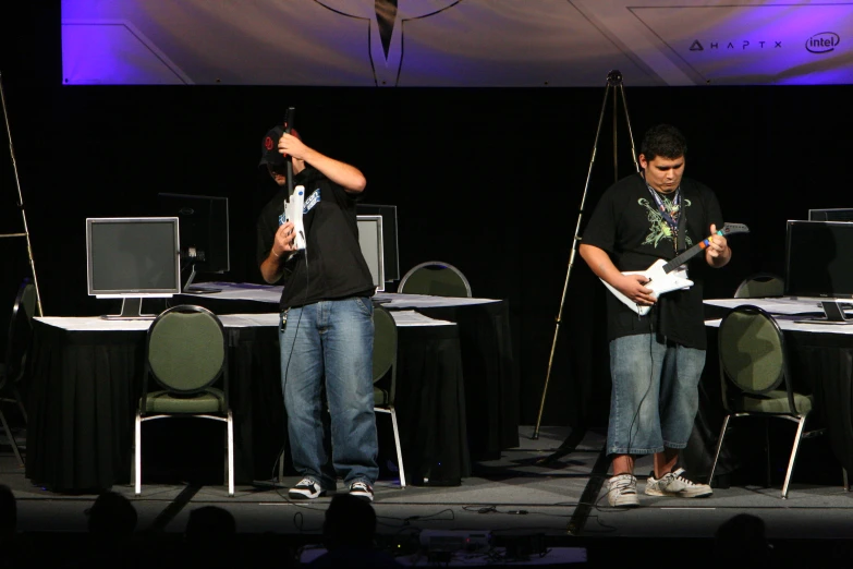 two young men standing on a stage holding electronic devices