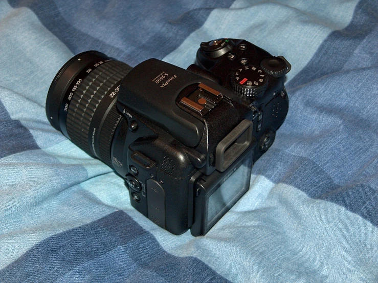 a black camera with a lens attached laying on a checkered blanket
