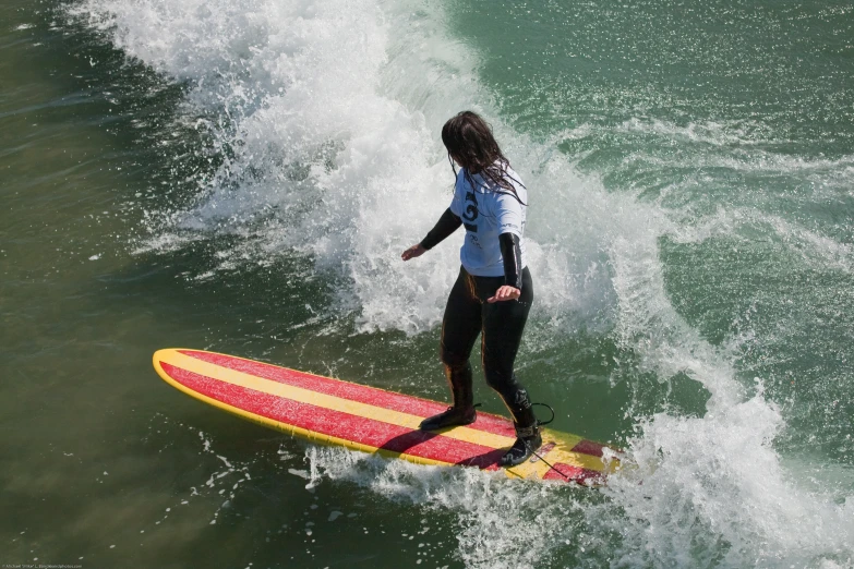 a woman standing on a yellow and red surf board while surfing