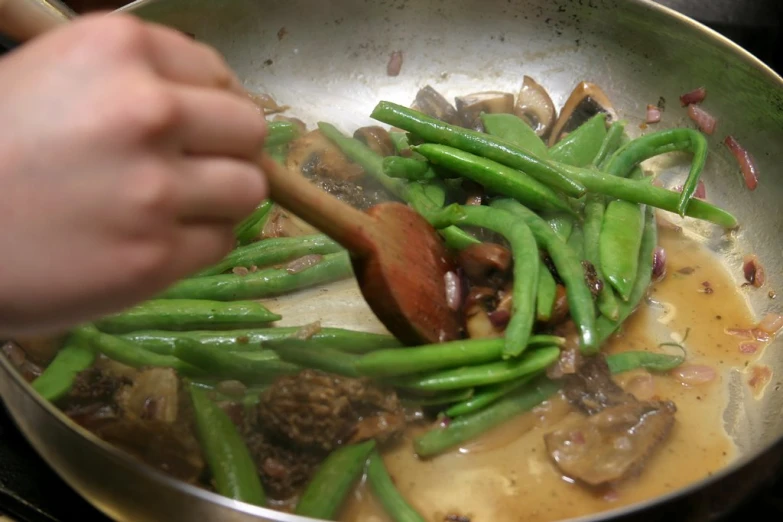 someone cooking green beans and mushrooms in a pan