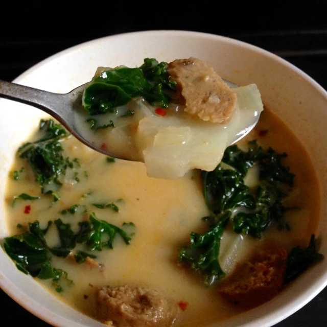 a white bowl full of meat, cheese and spinach soup