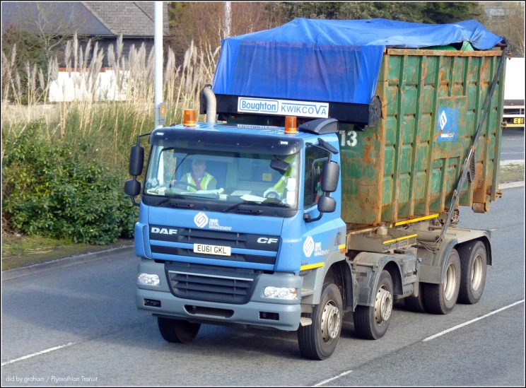 a dump truck driving down the road in front of some bushes