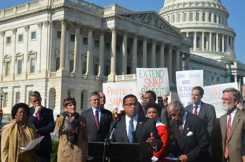 people at podium in front of capitol building holding signs and microphone