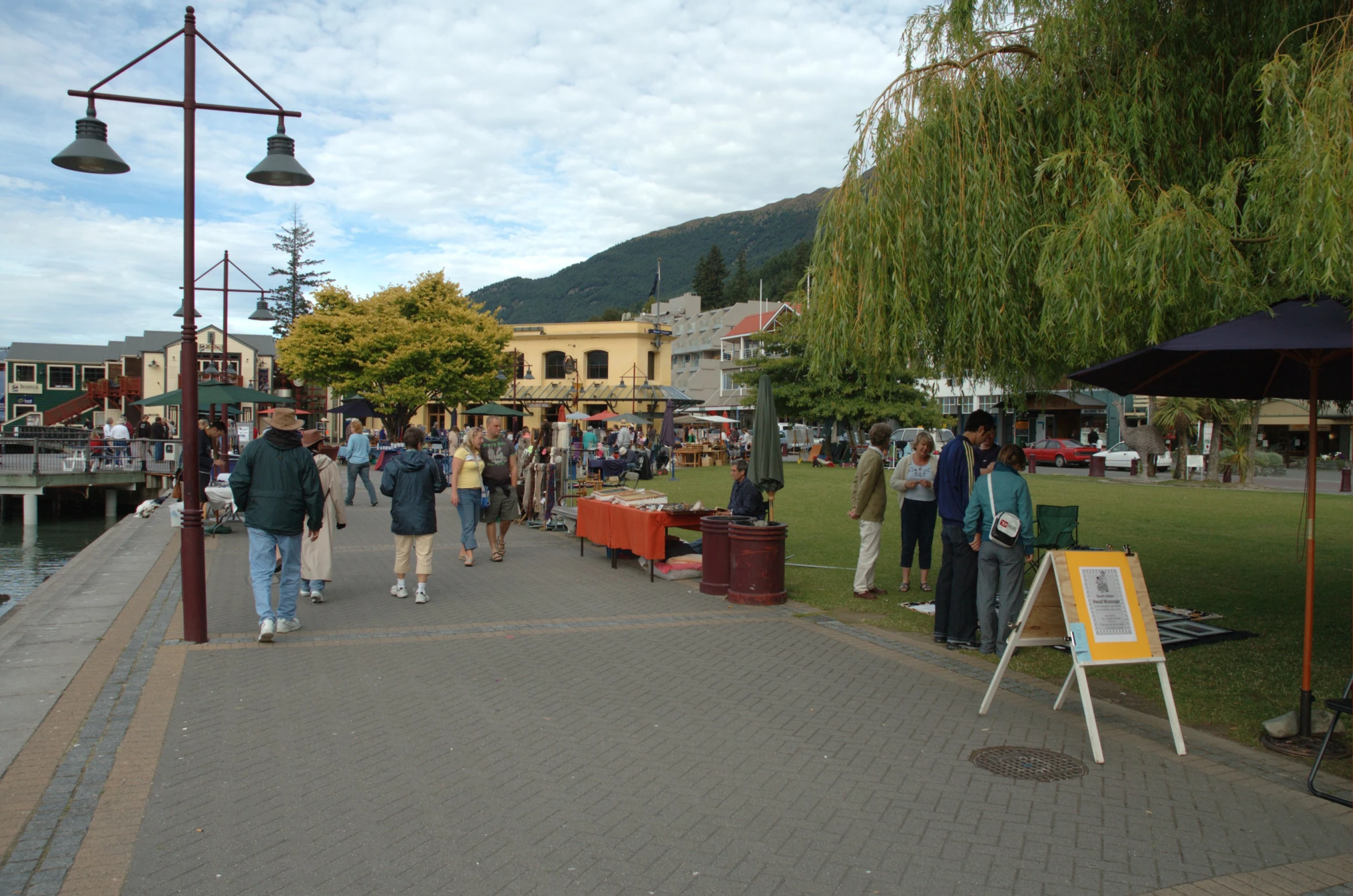 many people in an area near water, a sidewalk and a sign