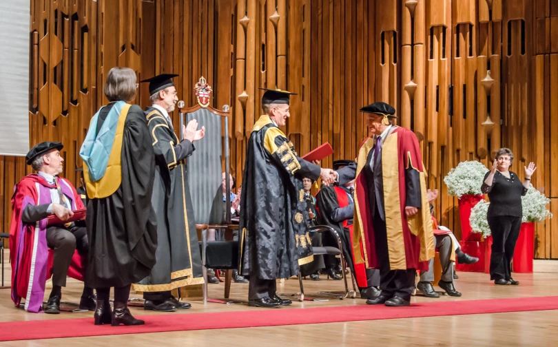 two graduates in robes of various ages stand on stage during the ceremony