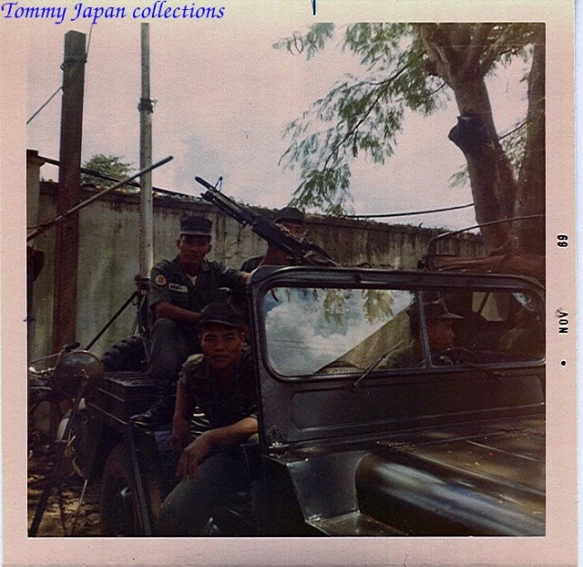 soldiers posing in the back of a truck with another vehicle nearby