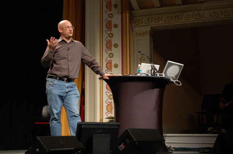 a man standing behind a podium with an open laptop on his lap