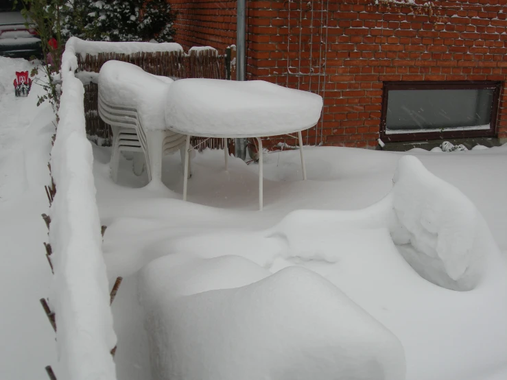 a snow covered lawn chair and table near brick building