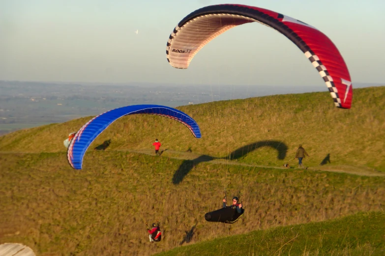 people paragliding on a grassy hill top