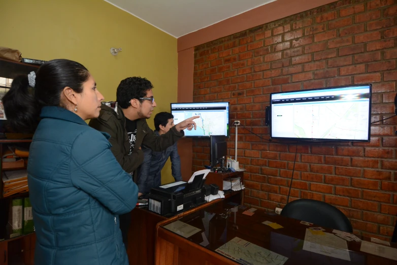 three people are watching a tv screen and other electronic equipment